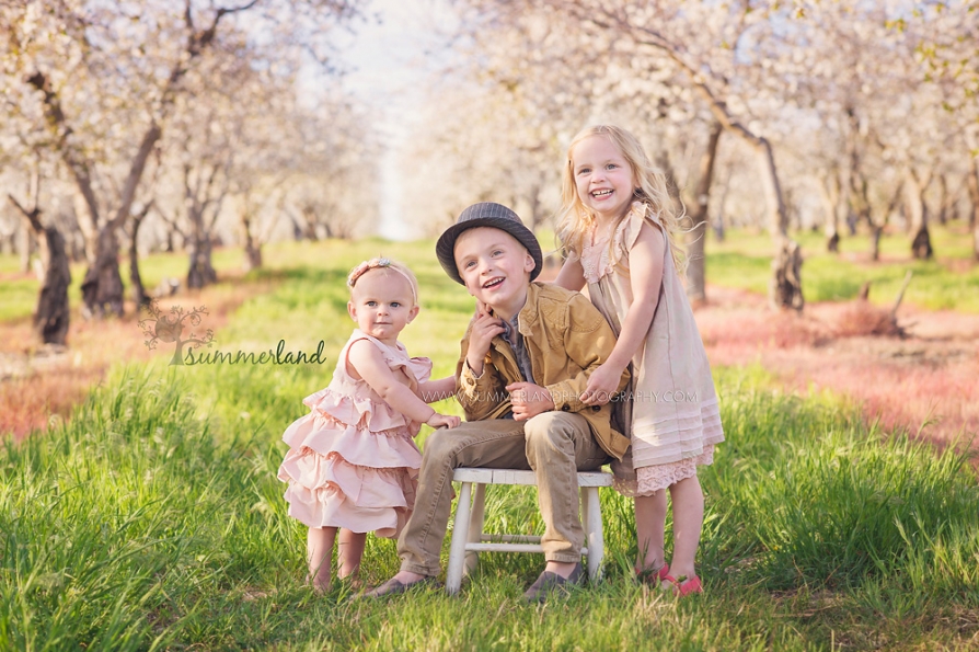 year old baby with older siblings in blooming apple orchard near Kennewick Washington